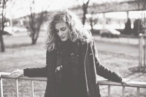 Hochzeitsreportage NRW – Braut mit Locken im Mantel am Geländer, draußen nach der Trauung.
