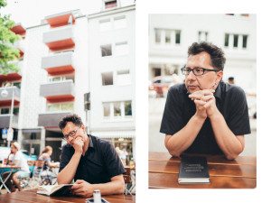 Ein Gast genießt einen ruhigen Moment an einem Cafétisch in Köln, während sich um ihn herum das Stadtleben entfaltet.