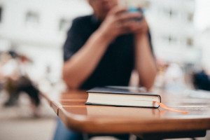 Auf einem Holztisch liegt ein geschlossenes Buch mit einer Schleife, im Hintergrund entspannte Café-Momente.