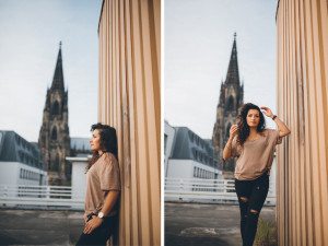 Braut lehnte entspannt an einer Mauer in Köln, der Dom verschwimmt sanft im Hintergrund.
