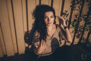 Sanftes Sonnenlicht streift das Gesicht einer Frau, die entspannt an einer Mauer sitzt – natürliche Portraitfotos Köln.