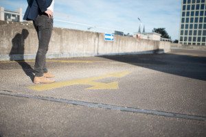 Eine Person bleibt auf dem Bürgersteig der Stadt neben einem gelben Pfeil stehen – urbane Bewerbungsfotos in Köln, locker und echt.