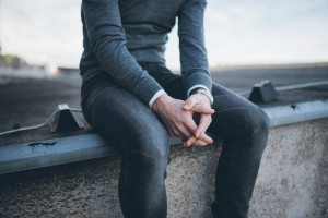 Person im grauen Pullover sitzt entspannt auf einer Mauer – natürliche Hochzeitsreportage NRW.