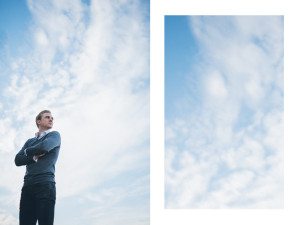 Eine Person in einem kuscheligen Pullover steht draußen unter sanften Wolken – natürliche Portraits in Köln.