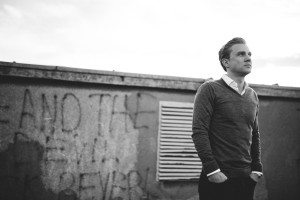 Ein Mann im Pullover lehnte an einer Kölner Wand – entspannte Bewerbungsfotos in urbanem Stil.