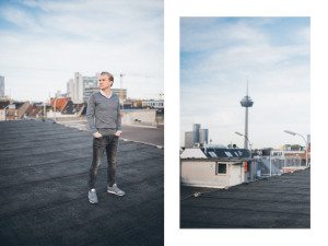 Ein Mann genießt entspannte Bewerbungsfotos auf einem Dach in Köln, mit Blick auf die Stadt und dem Fernsehturm dahinter.