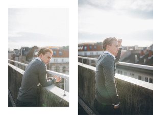 Ein Mann im grauen Pullover auf einem sonnigen Dach in Köln – moderne, authentische Portraitfotos.