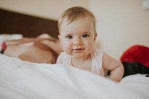 Baby mit blonden Haaren und blauen Augen liegt nach einer Strandhochzeit in Noordwijk entspannt auf einem Bett.