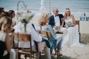 Brautpaar lächelt bei Strandhochzeit an der Nordsee, umgeben von Gästen – Hochzeitsreportage NRW.