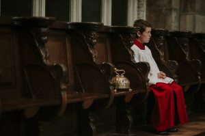 Junger Chorknabe in weiß-rotem Gewand sitzt bei standesamtlicher Trauung, Buch in der Hand.