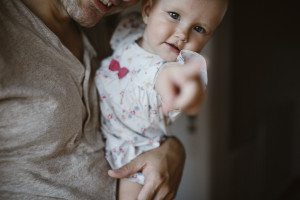 Herzlicher Moment bei Familienfotos Köln – ein Baby im geblümten Kleid zeigt neugierig in die Kamera.