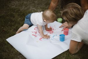 Kleines Kind malt bunte Handabdrücke auf Papier – liebevolle Familienfotos Köln draußen.