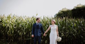Braut und Bräutigam halten Händchen vor einem Kornfeld – echte Hochzeitsmomente in NRW.