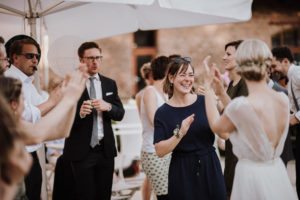 Gäste klatschen unter dem Baldachin auf Gut Hohenholz; Zwei Frauen teilen sich nach der standesamtlichen Trauung ein warmes Lächeln.