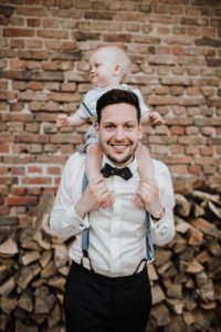 Ein Vater lächelt mit seinem Kind auf den Schultern bei einer Hochzeit auf Gut Hohenholz in NRW.