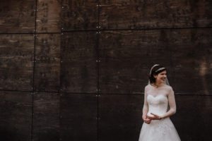 Braut im weißen Kleid lächelt entspannt vor Holzwand – Hochzeitsfotografin Köln fängt echte Momente ein.