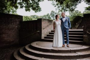 Ein Brautpaar steht lachend auf alten Steinstufen, liebevoll festgehalten von Hochzeitsfotografin Köln.