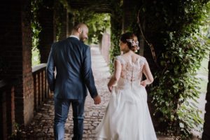 Brautpaar schlendert Hand in Hand unter grüner Pergola – Hochzeitsreportage NRW in natürlicher Atmosphäre.
