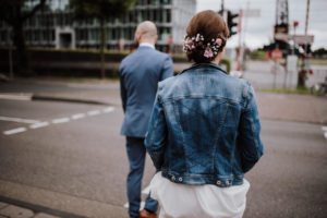 Braut mit Blumen im Haar und Jeansjacke, Bräutigam im blauen Anzug – entspannte Hochzeitsfotos Köln.