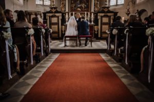 Braut und Bräutigam sitzen bei ihrer standesamtlichen Trauung, liebevoll umgeben von Gästen. Hochzeitsfotografin Köln hält echte Momente fest.