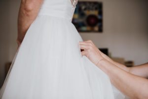 Eine sanfte Berührung richtet ein Hochzeitskleid während einer herzlichen Hochzeit im Schokoladenmuseum Köln.