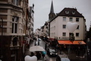 Zwei weiße Herzballons schweben an einem regnerischen Tag in der Kölner Innenstadt.