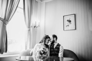 Brautpaar sitzt innig auf dem Sofa, lächelt und genießt echte Hochzeitsmomente in Köln.