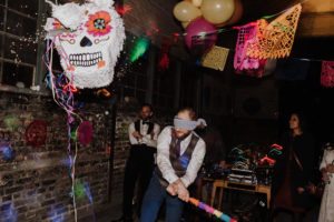 Ein Bräutigam mit verbundenen Augen lacht, während er versucht, eine Piñata zu schlagen – authentische Hochzeitsmomente in NRW.