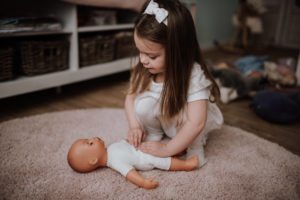 Ein kleines Mädchen spielt sanft mit ihrer Puppe auf einem weichen Teppich Doktor – Momente wie in der Hochzeitsreportage NRW.