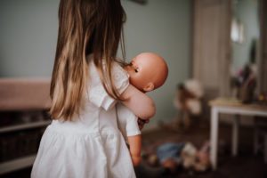 Ein kleines Mädchen im weißen Kleid wiegt ihre Puppe, spontaner Moment – Hochzeitsreportage NRW.