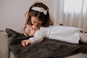 Ein junges Mädchen küsst sanft ein Baby in Weiß, ein offener Familienmoment – Hochzeitsreportage NRW.