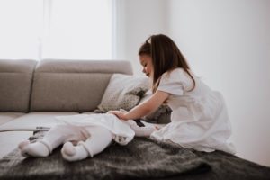 Ein Mädchen legt sanft ein Baby auf die Couch, festgehalten von Hochzeitsfotografin Köln.