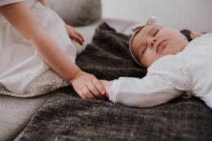 Die große Schwester hält sanft die Hand ihres neugeborenen Geschwisterchens – innige Momente, Hochzeitsreportage NRW.