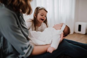 Eine Mutter hält ihr Baby, die große Schwester lächelt liebevoll – Hochzeitsreportage NRW.