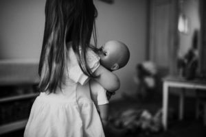 Kleines Mädchen hält liebevoll ihre Puppe im Zimmer – Momentaufnahme von Hochzeitsfotografin Köln.