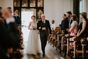 Eine Braut geht mit ihrem Vater lächelnd zum Altar – Hochzeitsreportage NRW, echte Emotionen.