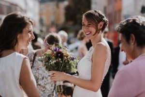 Braut im weißen Kleid lacht mit Freundinnen im Grünen – Hochzeitsreportage NRW natürliche Momente.