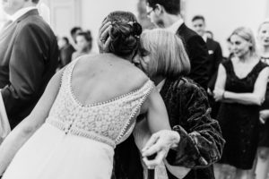 Eine Großmutter umarmt die Braut herzlich, umgeben von ihren Lieben – Hochzeitsfotografin Köln Moment.