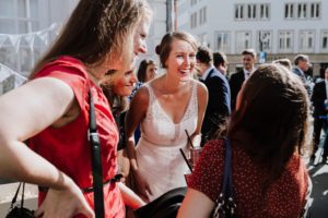 Braut im weißen Kleid lacht mit Freundinnen bei einer entspannten standesamtlichen Trauung in Köln.