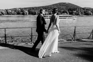 Ein Brautpaar spaziert Hand in Hand am Rheinufer – Hochzeitsreportage NRW mit natürlicher Freude.
