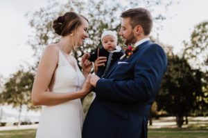 Brautpaar mit Baby im Arm, lachend im Grünen – echte Hochzeitsmomente in NRW festgehalten.