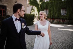 Brautpaar lächelt sich an und spaziert Hand in Hand auf Kopfsteinpflaster – Hochzeitsfotografin Köln.