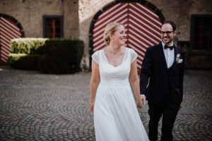 Braut und Bräutigam gehen Hand in Hand über Kopfsteinpflaster – Hochzeitsreportage NRW.