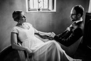 Braut und Bräutigam sitzen Hand in Hand auf dem Sofa – natürliche Hochzeitsfotografie Bonn.
