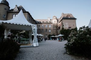Hochzeit im Freien in der Nähe eines historischen Steingebäudes, die Gäste versammelten sich unter weißen Zelten in üppigen grünen Gärten.