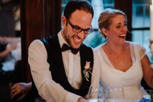 Brautpaar lacht herzlich zusammen am Tisch – natürliche Hochzeitsfotografie Bonn.