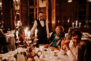 Ein lächelnder Kellner bedient die Gäste bei einem Hochzeitsessen bei Kerzenschein – natürliche Hochzeitsreportage Bonn.