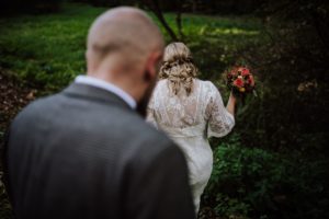 Braut im Spitzenkleid lächelt mit Blumenstrauß, Bräutigam in der Nähe – echte Hochzeitsmomente in Köln festgehalten.