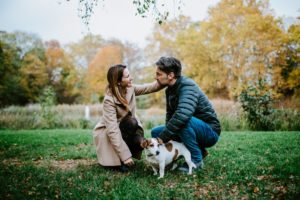 Ein Paar kniet mit seinem Hund im Herbstgras und lächelt – Hochzeitsfotografin Bonn.