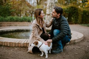 Brautpaar kniet lachend mit ihrem Hund am Brunnen im Park – echte Hochzeitsreportage NRW.